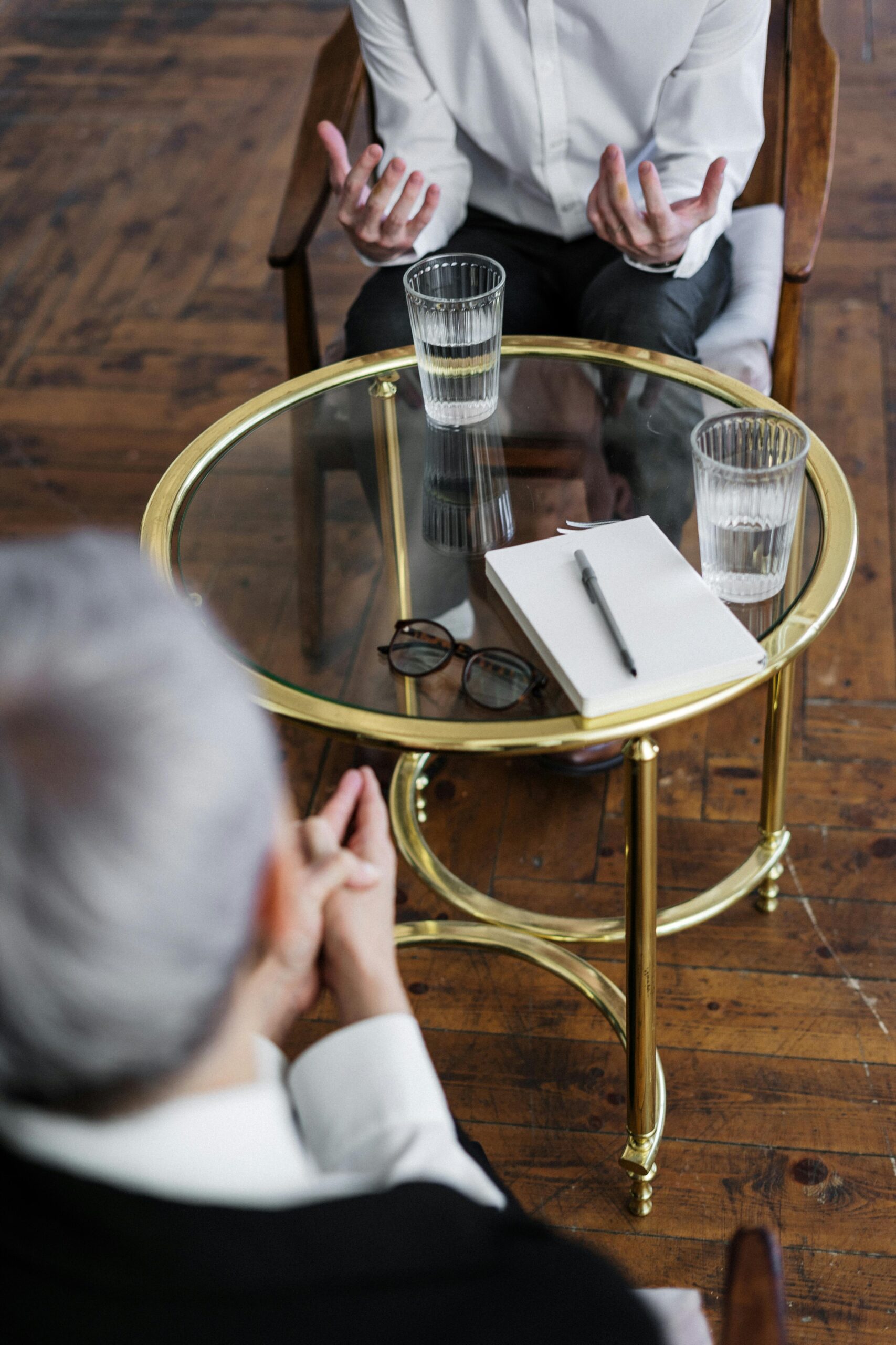 From above crop African American male in casual clothes sitting on comfy couch and answering professional female consultant questions in modern psychotherapy office